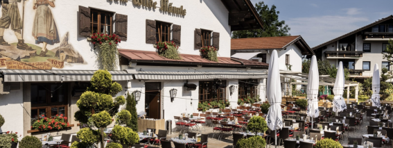 Ein traditionelles Restaurant in Bayern mit blühenden Pflanzen und einer großen Terrasse an einem sonnigen Tag.