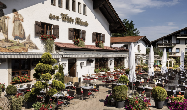Restaurant im bayerischen Stil mit schöner Terrasse Ein traditionelles Restaurant in Bayern mit blühenden Pflanzen und einer großen Terrasse an einem sonnigen Tag.