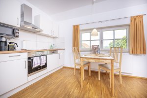 In einer Wohnung in Deutschland steht ein Tisch mit Stühlen in einer modernen Küche. Die Fenster lassen Licht herein.