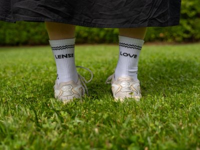 Eine Person steht im Gras und trägt sportliche Schuhe mit Socken, die die Worte LENSE und LOVE zeigen.