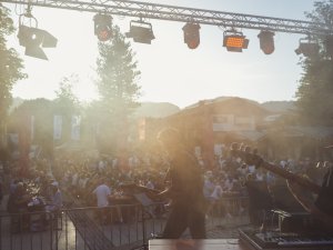 Menschen hören Musik während eines Konzerts im Freien. Die Bühne ist beleuchtet und es gibt viele Zuschauer vor der Bühne.