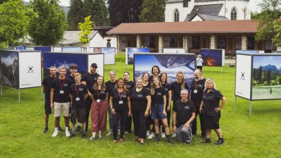 Menschen stehen im Freien und posieren vor Kunstwerken. Die Ausstellung findet am Tag in einem Park statt.