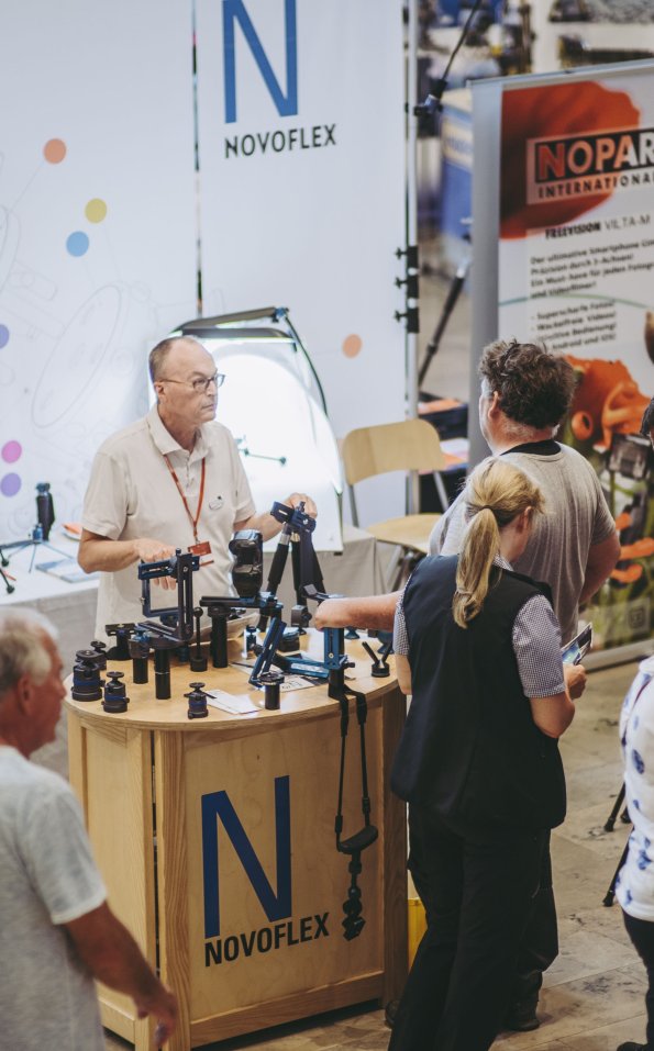 Menschen betrachten verschiedene Kameraausrüstungen beim Fotogipfel 2019 im Oberstdorf Haus. Ein Stand zeigt Produkte von Novoflex im Oberstdorf Haus.