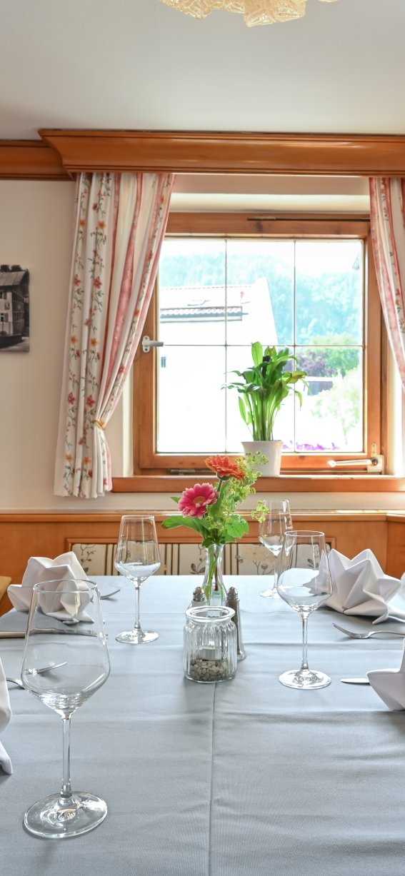 Im Restaurant steht ein schön gedeckter Tisch. Die Fenster sind hell und der Raum hat Holzverkleidung.