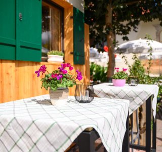 Das Restaurant hat Tische draußen mit Blumen im Topf. Menschen sitzen und essen auf der Terrasse. Es ist ein schöner Tag.