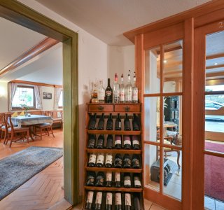 Der Eingangsbereich zeigt ein Holzregal mit Weinflaschen. Im Hintergrund sieht man Tische und Stühle.