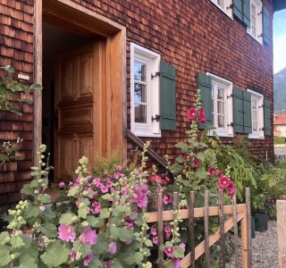 Eingangsbereich eines Holzhauses mit Blumen Der Eingang eines Holzhauses ist mit vielen Blumen geschmückt. Es ist ein klarer Tag, und die Pflanzen blühen.