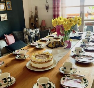 Der Tisch ist gedeckt mit Tassen, Tellern und einer großen Torte. Frühlingstulpen stehen in der Mitte.