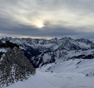 Sonnenaufgang über den Bergen im Winter Die Sonne geht über den schneebedeckten Bergen auf. Der Himmel ist grau und die Landschaft ist ruhig.