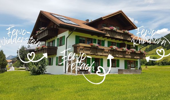 In der Bergregion gibt es ein großes Gebäude mit mehreren Ferienwohnungen. Es ist Sommer und die Wiesen sind grün.