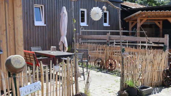 Ein einladender Innenhof mit Holzverkleidung, Gartentisch und Holzzäunen umgeben von Grünpflanzen und rustikalem Flair.