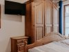 Im Raum stehen ein Bett, ein Kleiderschrank und eine Kommode. Der Fernseher ist an der Wand montiert. Holzmöbel im Schlafzimmer mit Fernseher an der Wand