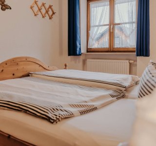 In einem Zimmer stehen zwei Betten. Ein Fenster lässt Licht herein. Die Wände zeigen einige Bilder und Dekorationen.