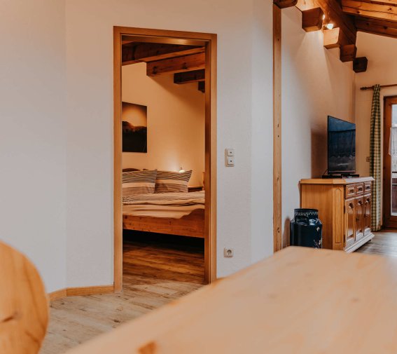 Wohnzimmer und Schlafzimmer in einer Wohnung Das Bild zeigt ein Wohnzimmer mit offenem Zugang zu einem Schlafzimmer in einer Wohnung. Es gibt Holzmöbel und ein Fenster.