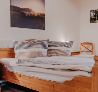 Schlafzimmer mit Holzbetten und Bildern an der Wand Das Zimmer hat zwei Holzbetten, Kissen, Bilder an der Wand und eine warme Atmosphäre. Es ist gut beleuchtet und einladend.