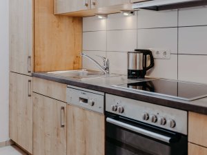 In der Küche stehen Holzregale, eine Kaffeemaschine und ein Herd. Die Geräte sind ordentlich angeordnet und funktionsfähig.