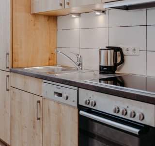 Moderne Küche mit Holzregalen und Geräten In der Küche stehen Holzregale, eine Kaffeemaschine und ein Herd. Die Geräte sind ordentlich angeordnet und funktionsfähig.