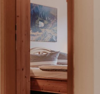 Der Raum zeigt ein Schlafzimmer mit einem Bett, Holzwänden und einem Bild an der Wand. Ein gemütlicher Ort zum Schlafen.