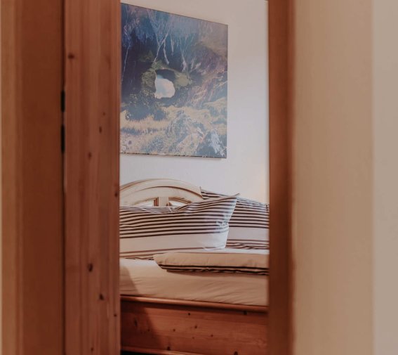 Der Raum zeigt ein Schlafzimmer mit einem Bett, Holzwänden und einem Bild an der Wand. Ein gemütlicher Ort zum Schlafen.
