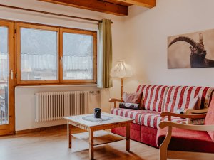 In einem Wohnbereich befindet sich ein rotes Sofa und ein Tisch. Es ist hell und ein Fenster zeigt die Berge draußen.