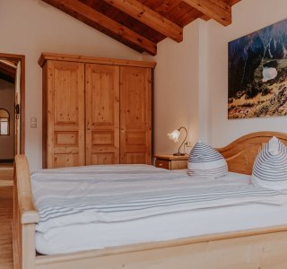 Ein Schlafzimmer mit einem großen Bett, Holzschränken und einem Bild. Es ist hell und hat eine gemütliche Atmosphäre.