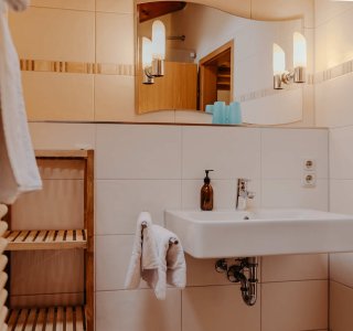 In einem Badezimmer steht ein Waschbecken mit einem Handtuch und einem Seifenspender. Die Wände sind hell.