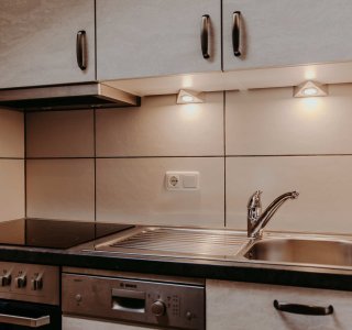 Die Küchenecke zeigt eine Spüle und einen Herd in einer Wohnung. Die Beleuchtung ist hell und die Oberfläche ist sauber.