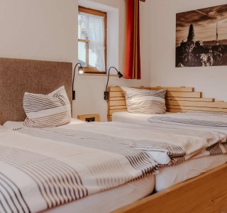 In einem Raum sind zwei Einzelbetten mit aufgeklappten Decken. Es gibt Fenster und eine Wanddekoration.