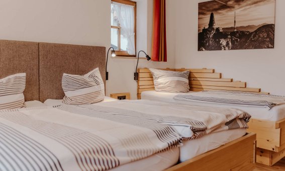 In einem Raum sind zwei Einzelbetten mit aufgeklappten Decken. Es gibt Fenster und eine Wanddekoration.