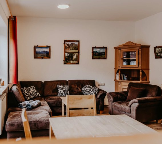 In einem Raum stehen bequeme Möbel. Bilder hängen an den Wänden. Ein Tisch ist in der Mitte des Raumes.