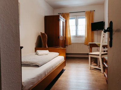 Helles Zimmer mit einem Bett, einem Schreibtisch und einem Kleiderschrank, ideal für einen ruhigen Aufenthalt.