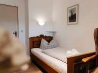 Ein helles Zimmer mit einem Einzelbett und einem bequemen Stuhl. Geeignet für Entspannung und Erholung.