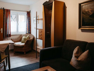 In einem hellen Raum stehen ein Sofa und ein Tisch. Es gibt einen gemütlichen Sessel und eine Kommode an der Wand.