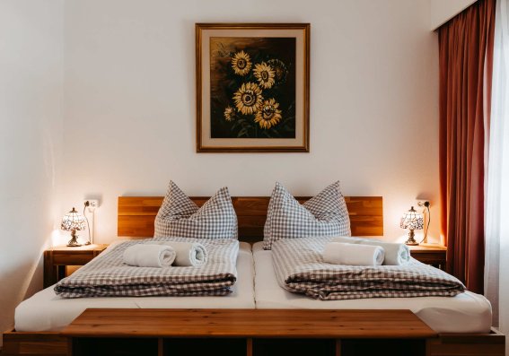 Doppelzimmer mit Blick auf die Sonnenblumen Ein gemüdliches Doppelzimmer mit zwei Betten, dekoriert mit einem Sonnenblumenbild. Sanfte Beleuchtung schafft eine einladende Atmosphäre.
