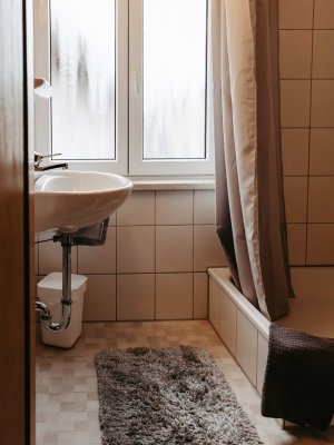 Im Badezimmer stehen ein Waschbecken und eine Badewanne. Draußen ist es bewölkt und die Fenster sind beschlagen.