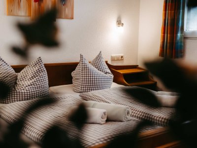 Ein gemütliches Schlafzimmer mit zwei Betten, karierten Kissen und handtuchgestapeltem Bettzeug in entspannter Atmosphäre.