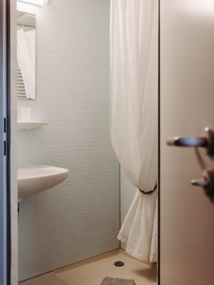 Der Raum zeigt eine saubere Dusche mit einem weißen Duschvorhang und frischen Handtüchern auf dem Boden.