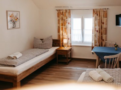 In einem hellen Zimmer stehen zwei Einzelbetten. Ein Tisch und ein Fenster sorgen für eine einladende Atmosphäre.