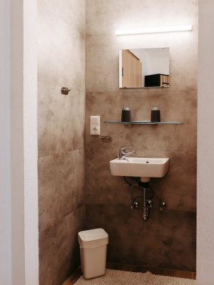 Kleines, modernes Badezimmer mit einem Waschbecken, Spiegel und einer Toilette in neutralen Farben.