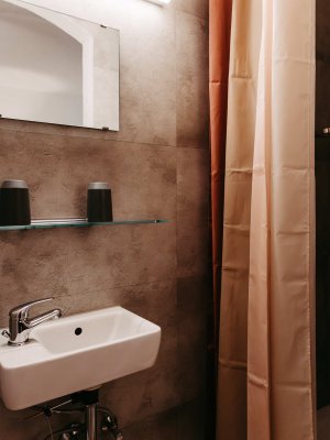 Hell erleuchtetes Badezimmer mit einem weißen Waschbecken, einem Spiegel und einem Duschvorhang zur Abtrennung.