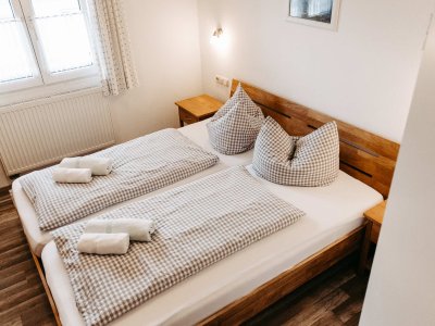 In diesem hellen Schlafzimmer stehen zwei Betten mit karierten Bettdecken. Handtücher liegen bereit.