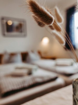 Im Schlafzimmer stehen zwei Betten, frische Pflanzen sind auf einem Tisch zu sehen, das Licht ist sanft und einladend.