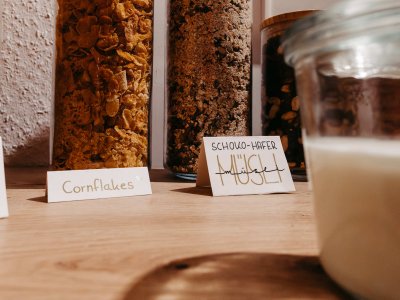 Verschiedene Getreidearten wie Cornflakes und Haferflocken stehen in einem stilvollen Küchenregal.