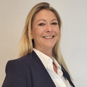 Eine lächelnde Geschäftsfrau präsentiert sich im modernen Büro. Sie trägt einen dunklen Blazer und strahlt Selbstbewusstsein aus. Professionelles Lächeln einer Geschäftsfrau im Büro