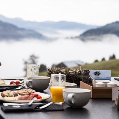 Ein Gast genießt das Bergfrühstück mit Blick auf Oberstaufen im Tal.