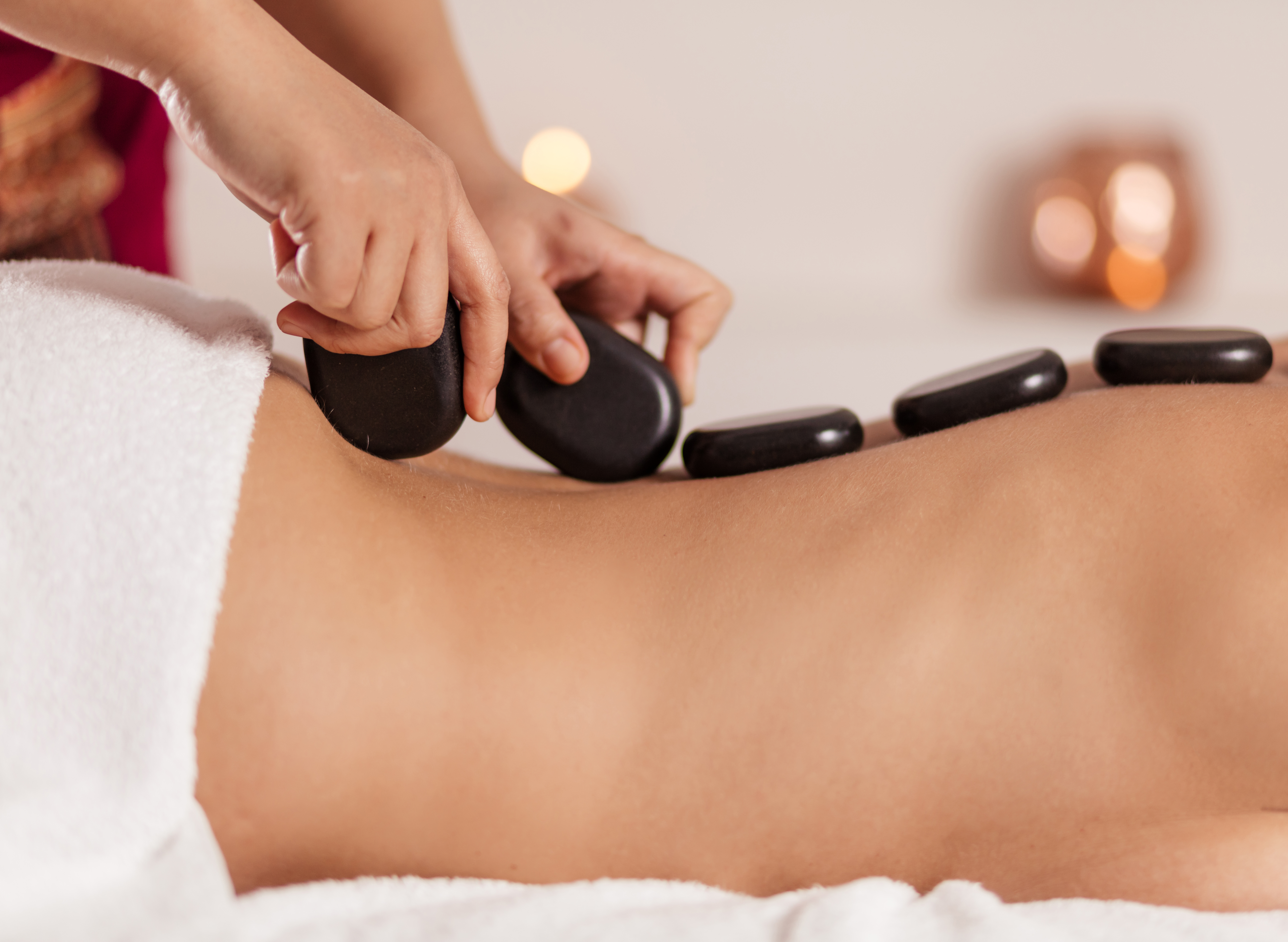Warme, glatte Steine werden bei der Hot-Stone-Massage auf der Wirbelsäule einer Haubers Gästin platziert.