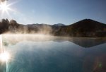 Über dem beheizten Infinitiy Pool des Wellnesshotels Allgäu steigen Dampfwolken vor den Alpenpanorama auf.