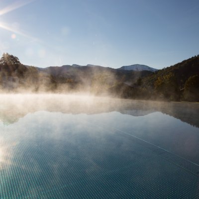 Über dem beheizten Infinitiy Pool des Wellnesshotels Allgäu steigen Dampfwolken vor den Alpenpanorama auf.