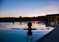 Ein Gast schwimmt in der Abendsonne im Außenpool des Last-Minute-Wellnesshotels im Allgäu.