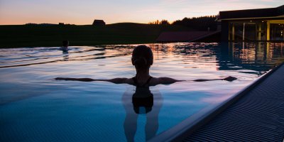 Ein Gast schwimmt in der Abendsonne im Außenpool des Last-Minute-Wellnesshotels im Allgäu.